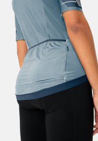 T-shirt de sport bleu clair avec une finition texturée, ourlet inférieur élastique et branding subtil, associé à un bas noir ajusté.