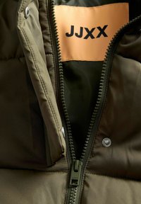 Puffer-jakke i olivengrøn med lynlås, inderside og et orange mærke med teksten "JJXX." Har en trykknapdetalje.