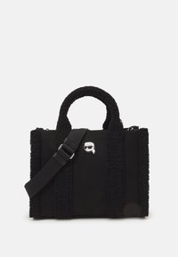 Fekete tote táska textúrált anyagból, plüss oldalsó részletekkel, rövid fogantyúkkal és állítható vállpánttal. Ezüst logómotívum látható.