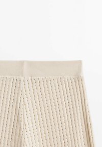 Beige textuurshorts met een geribd patroon, een elastische tailleband en kleine perforaties door de stof voor ademend vermogen.