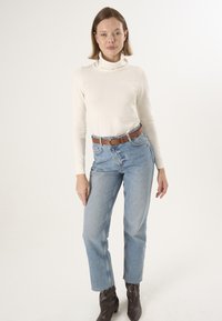 Pull encolure cheminée crème, jeans taille haute bleu clair, ceinture en cuir marron et bottines à talons pointus marron. Design simple, silhouette ajustée.