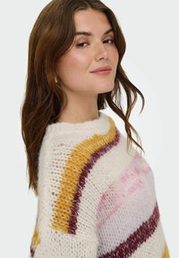 Strickpullover mit großzügigem Schnitt, cremefarbenem Grund und kräftigen horizontalen Streifen in Lila, Gelb und Pink. Strukturierte Webart verleiht Tiefe.