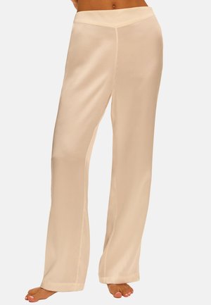 Beige wijde broek met een gladde textuur, blootsvoets gedragen door een persoon die van taille tot voeten is afgebeeld tegen een effen achtergrond.