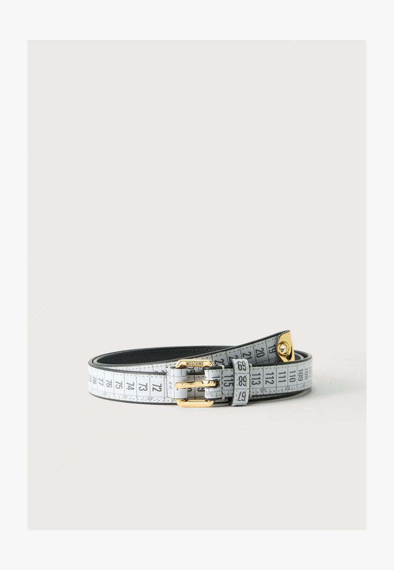 Ceinture blanche avec impression de ruban à mesurer et boucle dorée, posée à plat sur une surface blanche.