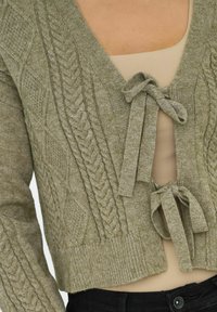 Cardigan en tricot vert olive avec des motifs de câbles texturés, décolleté en V et deux fermetures à nouer à l'avant, avec un ourlet et des poignets côtelés.