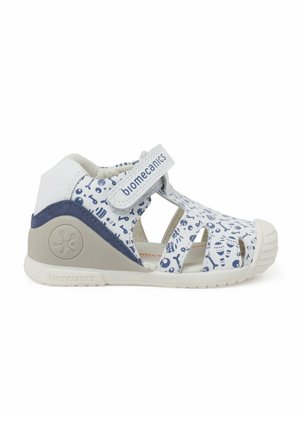 Sandalia blanca con parte superior de patrón azul y recortes. Cierre de tira de velcro y suela de goma gris con logo en el lateral.