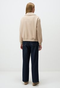 Beige bomberjack met een kraag en geribde cuffs, gecombineerd met donkerblauwe wijde spijkerbroek. Glad textuur met minimaal detail.