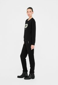 Mustan logo'iga sweatshirt, sobivad mustad dressipüksid dekoratiivsete nupukestega. Mudel kannab musti sääreülesandeid saapaid, millel on pannalakad.
