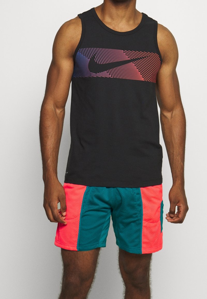 Homme musclé portant un débardeur noir avec des rayures colorées et un logo swoosh, associé à un short de sport turquoise vif et corail.