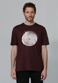Bordeauxfarbenes Baumwoll-T-Shirt mit einem kreisförmigen Baumring-Design in Hellgrau und umliegendem Text. Kurze Ärmel, Rundhalsausschnitt, lockere Passform.
