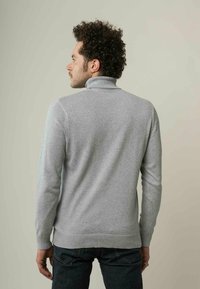 Grauer Rollkragenpullover aus Strickstoff mit geripptem Saum und Bündchen. Hat eine taillierte Passform. Wird über dunklen Jeans getragen, von hinten gezeigt.