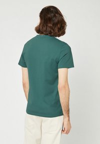 T-shirt in cotone verde con maniche corte, colletto rotondo e design minimalista, mostrato da dietro.