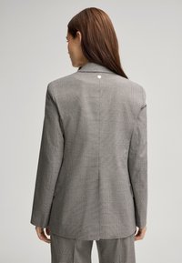 Grijze geruite blazer met een gestructureerd ontwerp, met notch-kleppen en een decoratieve knoop op de rug. Fijn afgestemde pasvorm met een subtiele textuur.