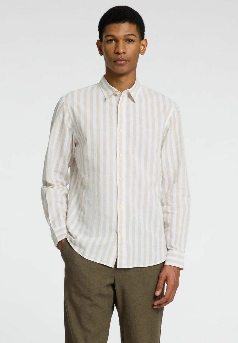 Camisa de rayas de color claro hecha de tela texturizada, con cuello puntiagudo, cierre de botones en la parte delantera y mangas largas. Llevada con pantalones de color oliva.