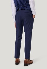 Marineblaue Anzughosen mit schmaler Passform, feiner Textur, seitlichen Taschen und geknöpften Gesäßtaschen, kombiniert mit braunen Schnürschuhen.