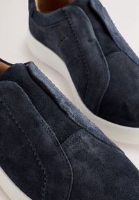 Baskets bateau en daim bleu marine sans lacets, avec semelles en caoutchouc blanc, détails cousus et col rembourré.
