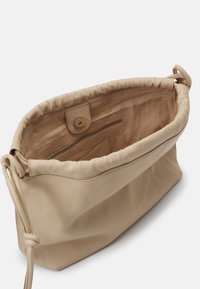 Beige kožená taška s měkkým, texturovaným povrchem a staženým vrškem. Uvnitř se nachází zipová kapsa a uzávěr na knoflík.