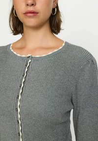 Grau gerippter Cardigan mit gewelltem Ausschnitt und vorderem Knopfverschluss. Lange Ärmel mit leichtem Puff. Strukturierter Strickstoff.