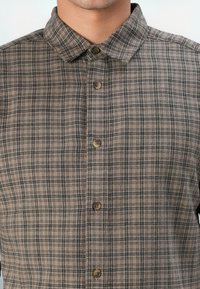 Brown plaid button-up shirt featuring a spread collar, front buttons, and a textured fabric with black and beige lines.