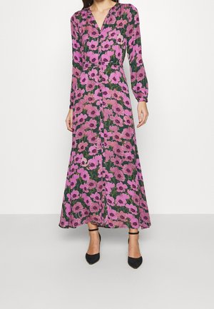 Mujer que lleva un vestido floral de manga larga hasta el tobillo con flores rosas y hojas verdes, combinado con tacones negros con correa en el tobillo.