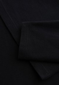 Primer plano de tela negra con costuras visibles y un borde doblado, destacando la textura y los detalles de la costura.