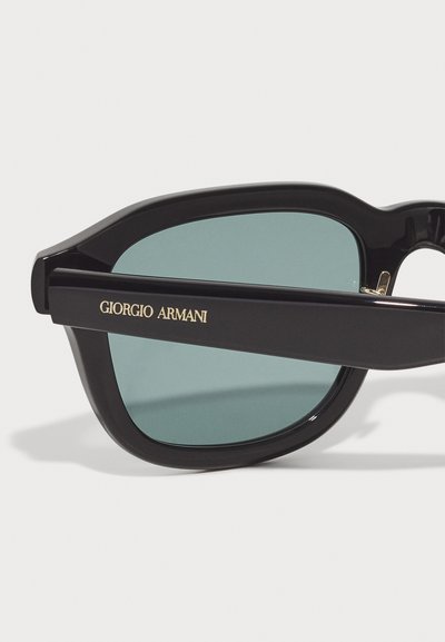 Ochelari de soare negri cu lentile verzi. Ramele au un finisaj lucios și un logo auriu "Giorgio Armani" pe templu.
