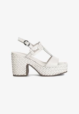 White platform sandals with woven textured heel, adjustable ankle strap, and T-bar design. Smooth material and padded footbed for comfort.