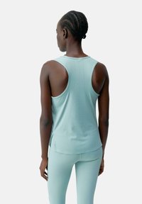 Lichtblauw sporttanktop met grote armsgaten, gebogen zoom en subtiele perforaties aan de achterkant, gecombineerd met bijpassende leggings.