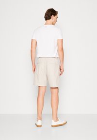 Lichtbeige shorts met een elastische tailleband en twee achterzakken, gecombineerd met een eenvoudig wit T-shirt en witte sneakers met rubberen zolen.