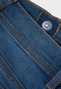 Denim tkanina u tamnoplavoj boji s narančastim šavom, s kopčanjem na gumb i dizajnom savijenog struka. Glatka tekstura s klasičnim izgledom.
