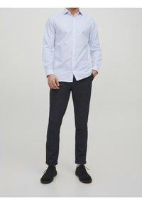 Jasnoniebieska koszula z długim rękawem z guzikami w połączeniu z ciemnymi, tapered spodniami i czarnymi butami. Tkanina wygląda na gładką i ma dopasowany krój.