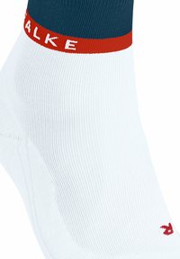 Calzino bianco alla caviglia con un risvolto teal e una banda rossa. Presenta testo del logo rosso e una texture liscia. Aree del tallone e della punta rinforzate.