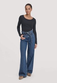 Zwarte lange mouw top met een ronde hals, gecombineerd met hoog-wijze wijde blauwe denim jeans met een strikgordel en textuurstof.