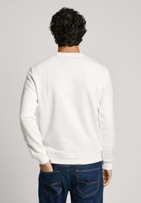 Sudadera de algodón blanca con cuello redondo, mangas largas y puños acanalados, combinada con jeans de mezclilla azul oscuro.