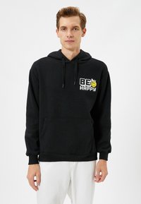 Sudadera negra de mezcla de algodón con un bolsillo frontal, capucha con cordón y un gráfico colorido con el texto "SÉ FELIZ."