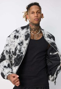 Veste bomber noir et blanc avec un design de texture peint, fermeture éclair et poignets côtelés. Portée sur un débardeur noir.