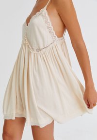Cremfarbener Sommerkleid mit strukturiertem Stoff, Spitzelementen und einem ausgestellten Rock, verstellbaren Trägern und einem tiefen V-Ausschnitt.