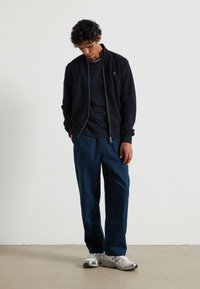 Jacket de marina con cremallera, camiseta de cuello redondo y pantalones azules holgados. Zapatillas plateadas con detalles texturizados. Diseño simple y moderno.