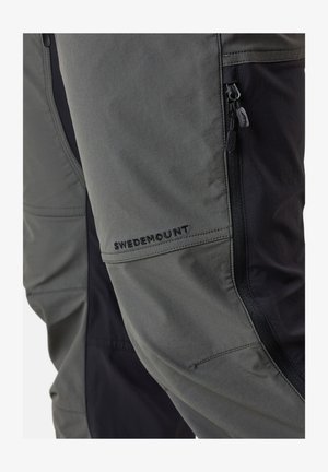 Zweifarbige Outdoor-Hosen aus grauem Stoff mit schwarzen Akzenten, mit Reißverschlusstaschen und dem gestickten "SWEDEMOUNT"-Logo an der Seite.