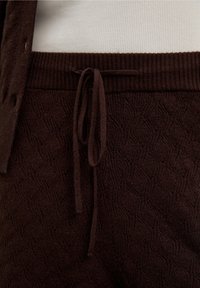 Pantalones marrones de punto con un patrón de ondas texturizadas, con una cintura elástica acanalada y cordón a juego. Material suave que ofrece comodidad.