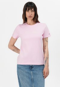 Rožinė medvilninė trumpomis rankovėmis marškinėliai su "Tommy Hilfiger" aukso spalvos logotipu. Audinys yra lygus, su klasikiniu apvaliu kaklu.