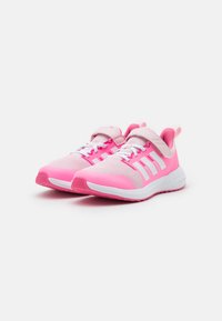 Scarpe da ginnastica rosa con una tomaia in rete traspirante, lacci bianchi e una cinghia in velcro. Presentano strisce bianche sui lati e una suola texturizzata.