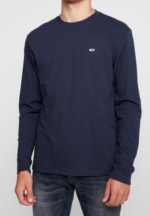 Marineblaue langärmelige Baumwollshirt mit Rundhalsausschnitt und kleinem Logo-Patch auf der linken Brust. Glatte Textur, lässige Passform.