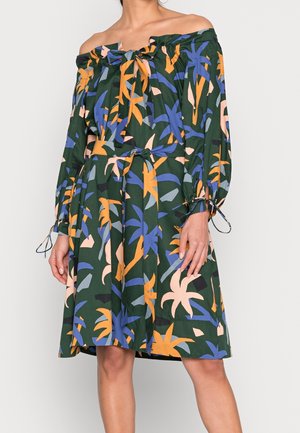 Robe épaules dénudées avec manches longues et un lien au niveau du col et de la taille, avec un motif de feuilles tropicales en bleu, orange et beige sur fond vert foncé.