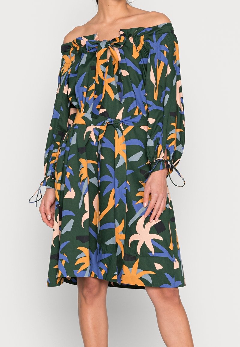 Robe épaules dénudées avec manches longues et un lien au niveau du col et de la taille, avec un motif de feuilles tropicales en bleu, orange et beige sur fond vert foncé.