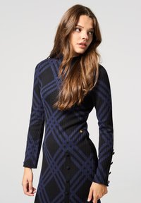 Abito a maniche lunghe nero e blu navy con una texture a coste, motivo geometrico, dettagli a bottone sulle maniche e una silhouette aderente.