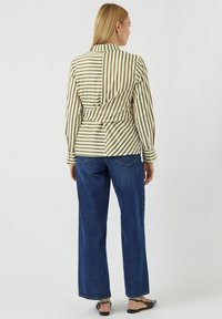 Gestreepte blouse in beige en olijf, met een strikdetail op de rug; gecombineerd met wijde blauwe denim jeans en zwarte platte sandalen.