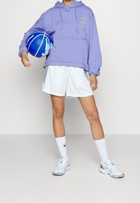 Violetti lyhyt huppari, jossa on etutasku, yhdistetty valkoisiin urheilushortseihin. Valkeat lenkkarit, joissa on kuvioitu pohja, ja valkoiset sukat. Sininen koripallo.