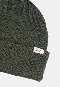 Berretto lavorato a maglia verde oliva con risvolto e una piccola etichetta bianca con un logo. Presenta una texture a coste su tutta la superficie.