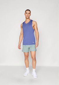 Fialový tílko bez rukávů s logem; světlé zelené šortky; bílé sportovní boty; hladká látka; volnější střih; jednoduchý design s minimálními detaily.